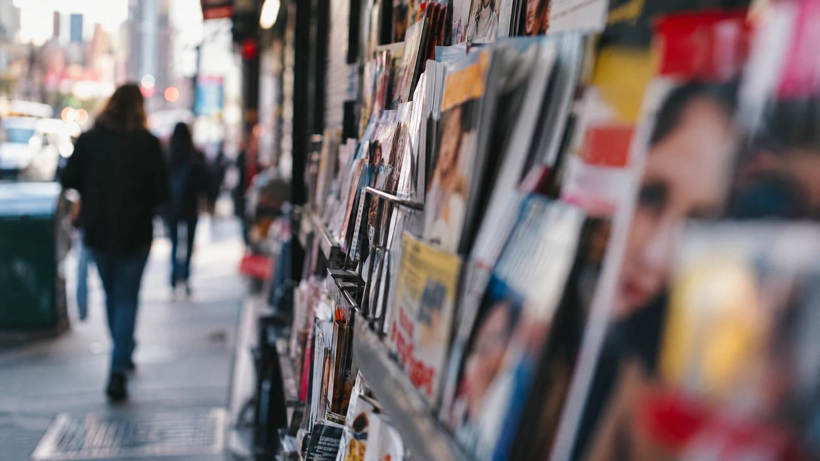 A rack of entertainment magazines softens into abstraction on a city street.