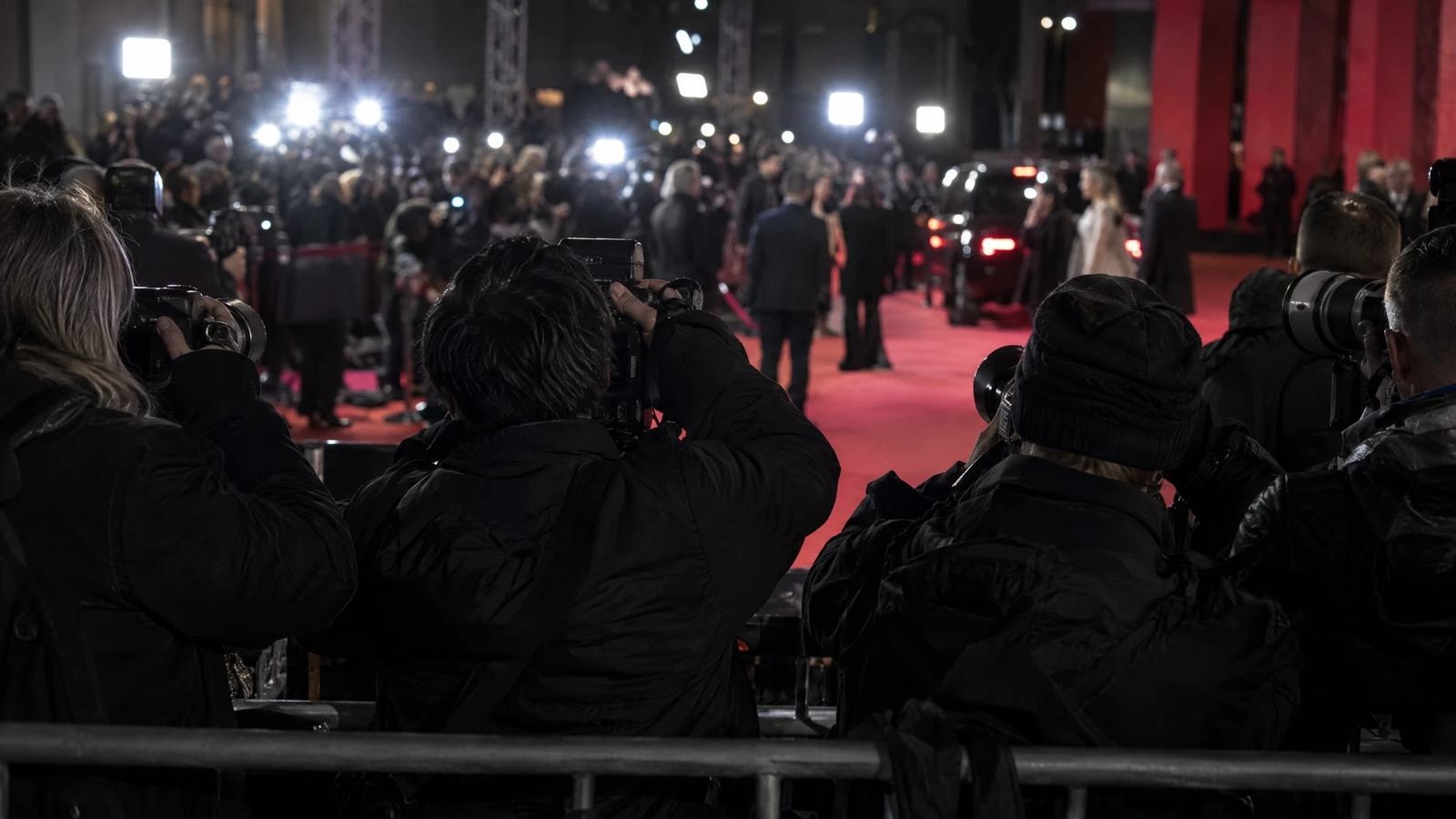 Photographers wait behind a barrier before a fictional film premiere.